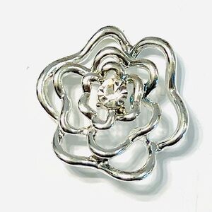 This is a silver-tone hollow flower lapel pendant with a crystal center.